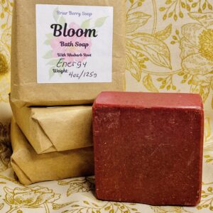 Bars of Bloom bath soap, three wrapped in brown paper and labeled, and one unwrapped showing its merlot coloring.