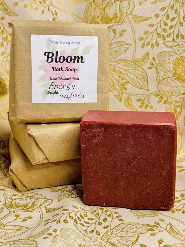 Bars of Bloom bath soap, three wrapped in brown paper and labeled, and one unwrapped showing its merlot coloring.