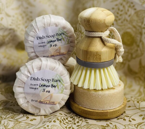 Dish soap bars wrapped and labeled and one bar unwrapped resting on a soap dish with a scrub brush on top.