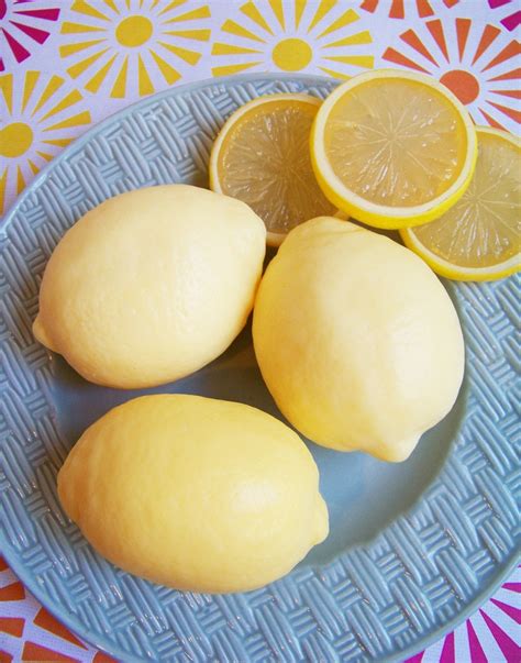 Lemons and lemon slices on a white basket weave plate on a pink, yellow and orange tablecloth.